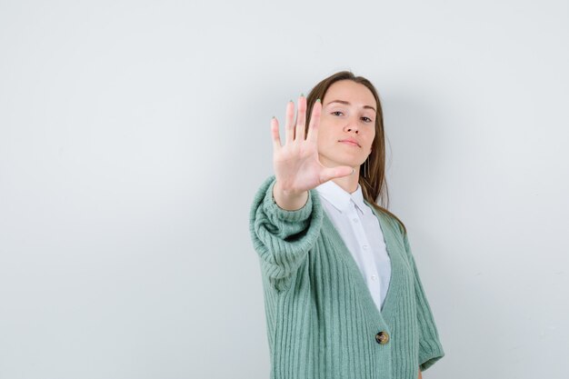 Jeune femme montrant un geste d'arrêt en chemise, cardigan et l'air confiant, vue de face.