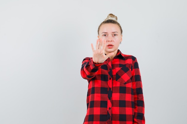 Jeune femme montrant le geste d'arrêt en chemise à carreaux et à la peur. vue de face.