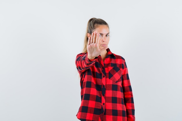 Jeune femme montrant le geste d'arrêt en chemise décontractée et à la recherche de sérieux. vue de face.