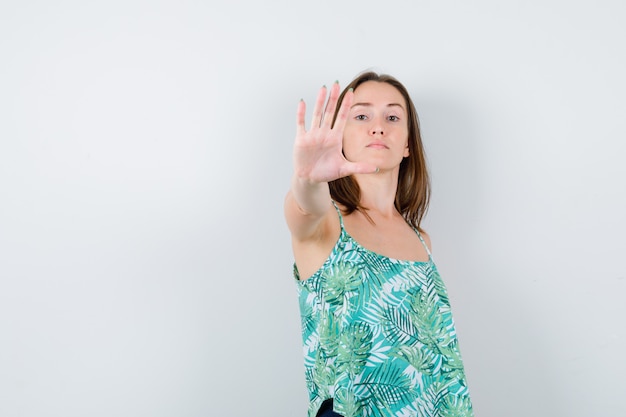 Jeune femme montrant un geste d'arrêt et semblant confiante, vue de face.