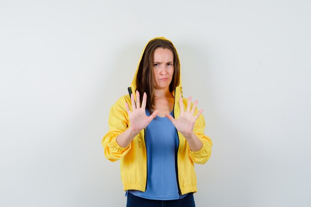 Jeune femme montrant un geste d'arrêt en t-shirt, veste et semblant sérieuse. vue de face.