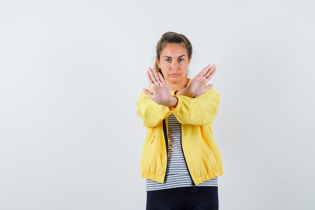 Jeune femme montrant le geste d'arrêt en veste, t-shirt et à la vue de face, confiant.