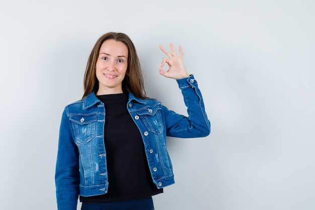 Jeune femme montrant un geste correct en blouse, veste et l'air confiant. vue de face.