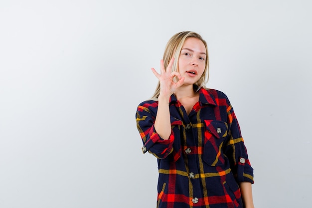 Jeune femme montrant un geste correct en chemise à carreaux et à la recherche de confiance. vue de face.