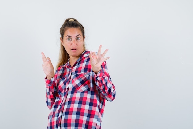 Jeune femme montrant un geste correct en chemise à carreaux et à la surprise. vue de face.