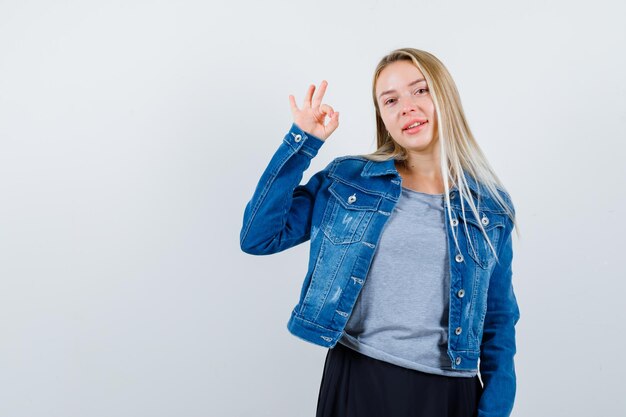 Jeune femme montrant un geste correct en t-shirt, veste en jean, jupe et l'air heureux