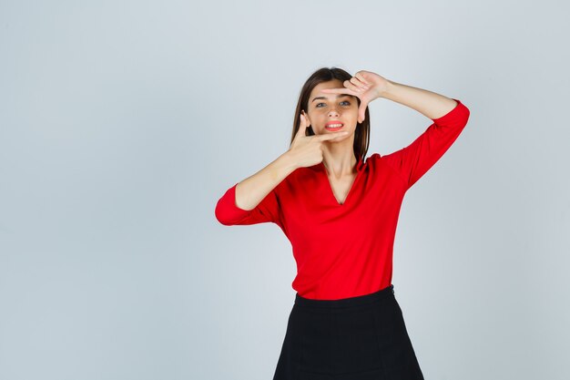 Jeune femme montrant le geste du cadre en chemisier rouge, jupe noire et à la joyeuse