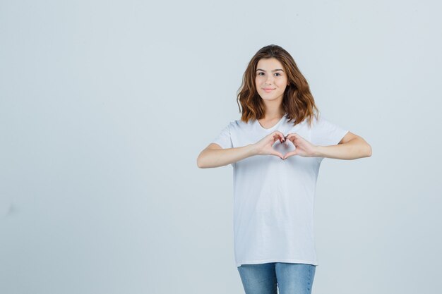 Jeune femme montrant le geste du cœur en t-shirt, jeans et jolie. vue de face.