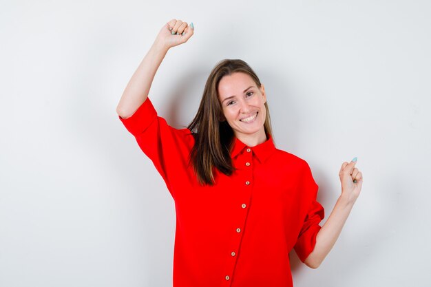 Jeune femme montrant le geste du gagnant en blouse rouge et l'air heureux. vue de face.