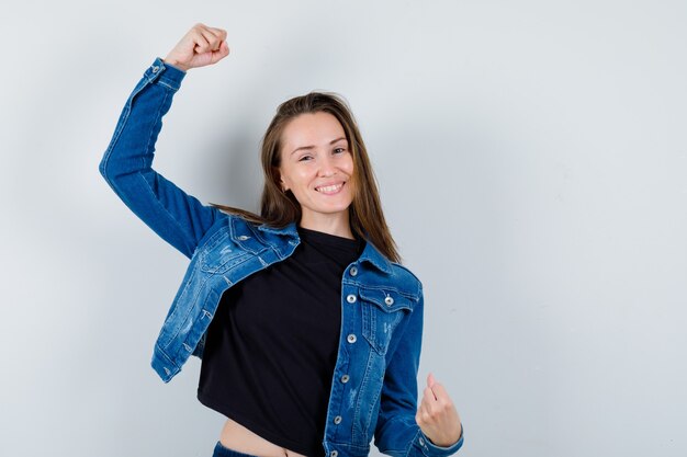 Jeune femme montrant le geste du gagnant en blouse, veste et l'air heureuse. vue de face.