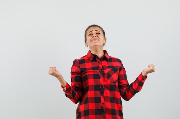 Jeune femme montrant le geste du gagnant en chemise à carreaux et à la chance.