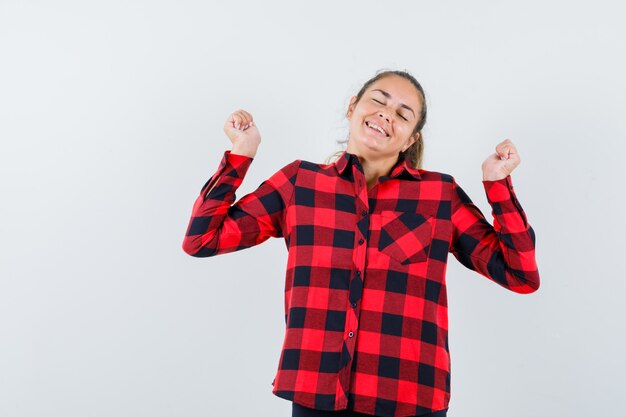 Jeune femme montrant le geste du gagnant en chemise à carreaux et à la recherche de plaisir