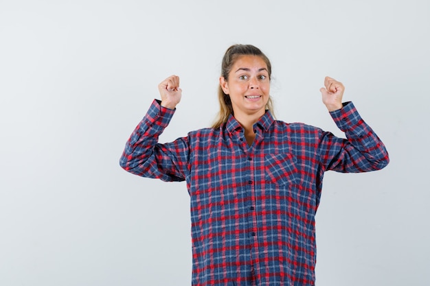 Photo gratuite jeune femme montrant le geste du gagnant en chemise à carreaux et à la recherche de plaisir