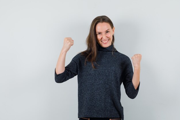 Jeune femme montrant le geste du gagnant en chemise et à la recherche de plaisir. vue de face.