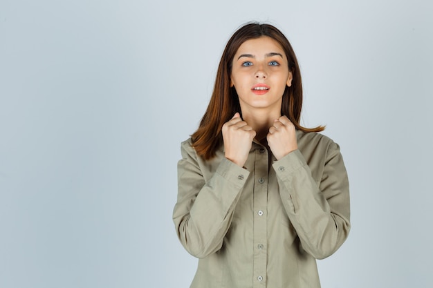 Jeune femme montrant le geste du gagnant en chemise et semblant chanceuse, vue de face.