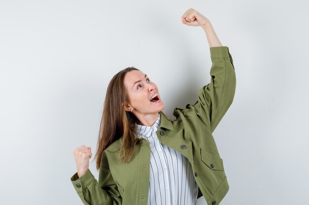 Jeune femme montrant le geste du gagnant en chemise, veste et à la chance, vue de face.