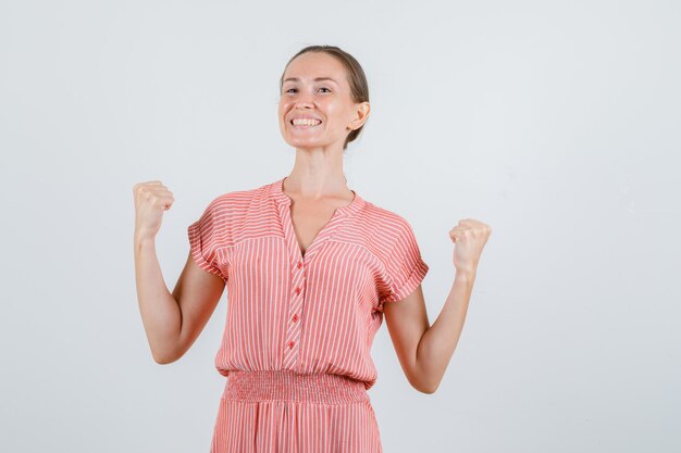 Jeune femme montrant le geste du gagnant en robe rayée et à la vue de face, heureux.