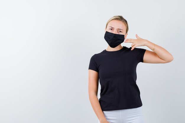 Jeune femme montrant le geste du pistolet en t-shirt, pantalon, masque médical isolé