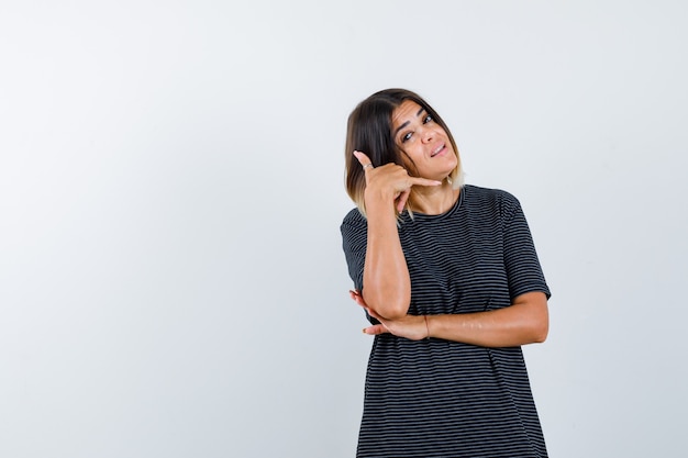 Jeune femme montrant le geste du téléphone en robe de polo et à la confiance. vue de face.