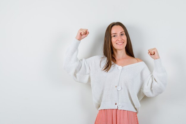 Jeune femme montrant le geste gagnant en cardigan et jupe à heureux isolé