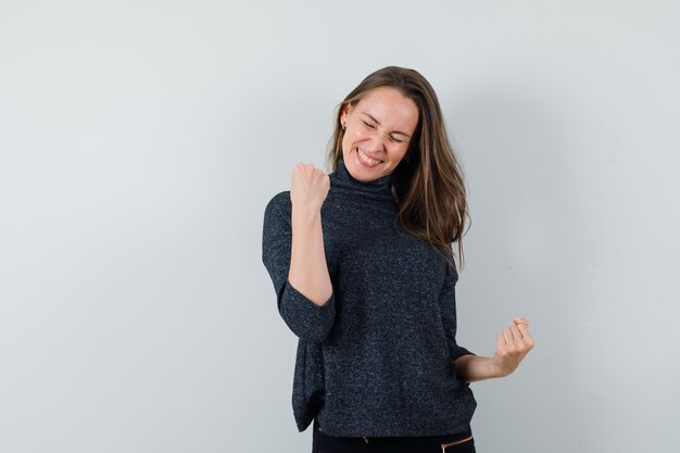 Jeune femme montrant le geste gagnant en chemise et à la béatitude. vue de face.