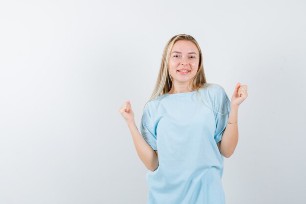 Jeune femme montrant le geste gagnant en t-shirt et à la béatitude, vue de face.