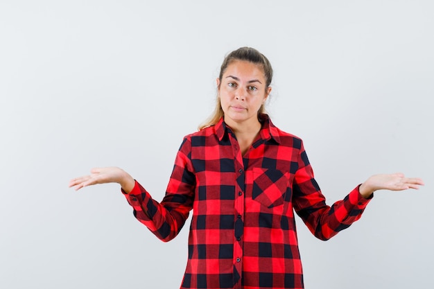 Jeune femme montrant un geste impuissant en chemise à carreaux et à la confusion