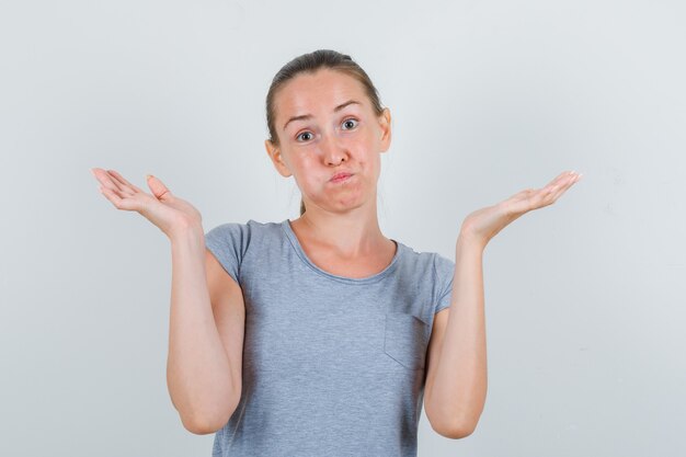 Jeune femme montrant un geste impuissant en t-shirt gris et à la confusion. vue de face.