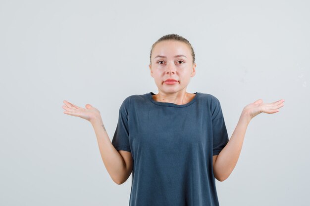 Jeune femme montrant un geste impuissant en t-shirt gris et à la confusion