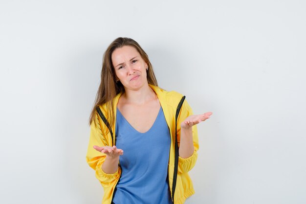 Jeune femme montrant un geste impuissant en t-shirt et semblant confuse. vue de face.