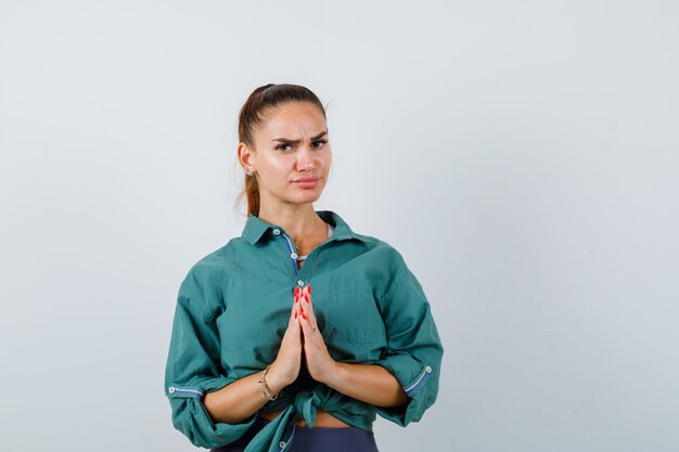 Jeune femme montrant le geste de namaste en chemise verte et à la réflexion, vue de face.