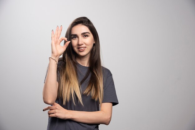 Jeune femme montrant le geste ok et debout sur un fond gris.