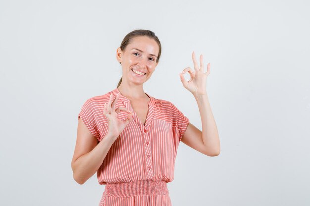 Jeune femme montrant le geste ok en robe rayée et à la joyeuse, vue de face.