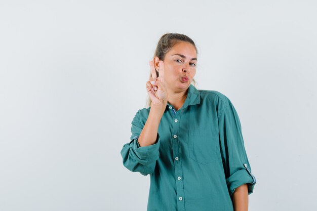 Jeune femme montrant le geste de paix en chemisier vert et à la recherche attrayante