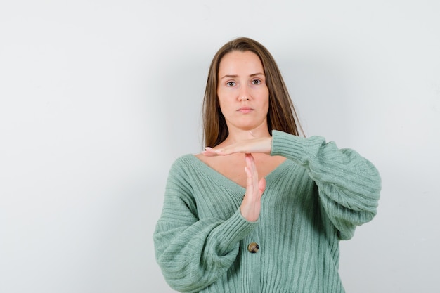 Jeune femme montrant le geste de pause dans le cardigan de laine et à la sérieuse. vue de face.