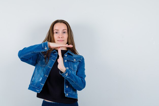 Jeune femme montrant un geste de pause dans le chemisier, une veste et l'air confiant, vue de face.