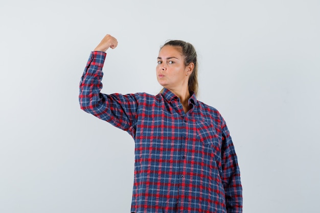Jeune femme montrant le geste de puissance en chemise à carreaux et à la recherche de puissance