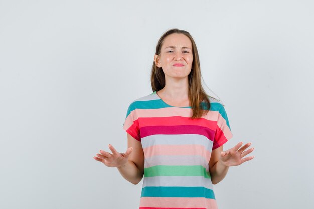 Jeune femme montrant le geste de ralentir avec les paumes en t-shirt et à la détente. vue de face.