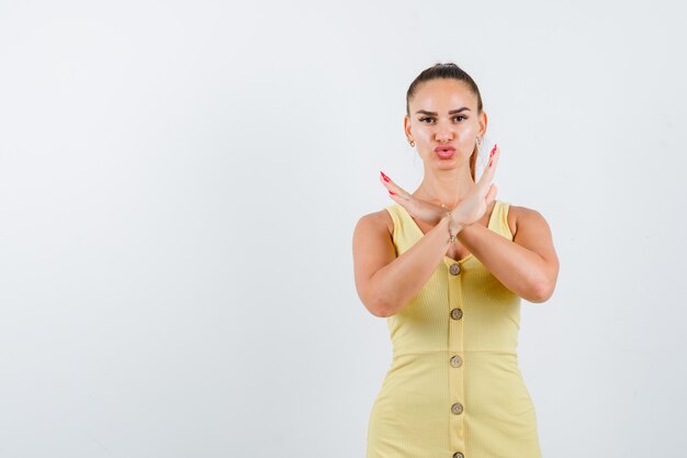 Photo gratuite jeune femme montrant un geste de refus en robe jaune et à la vue de face, confiant.