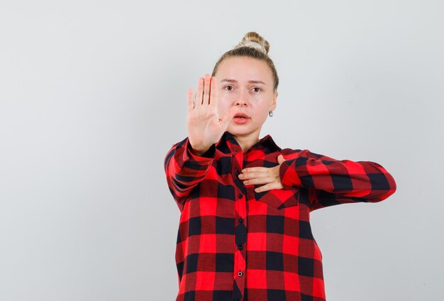 Jeune femme montrant un geste de refus en se pointant en chemise à carreaux. vue de face.