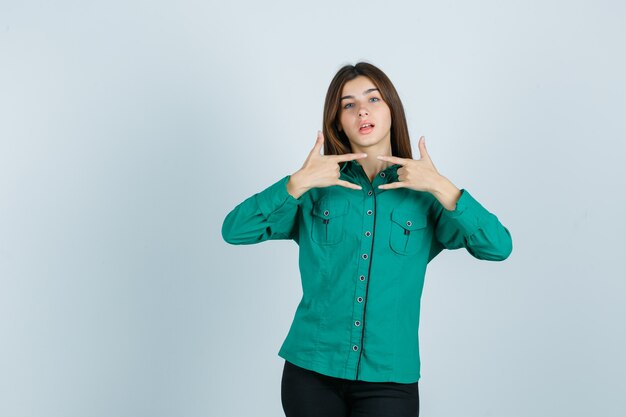 Jeune femme montrant le geste de la roche en chemise verte et à la vue de face, confiant.