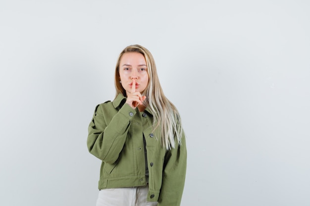 Jeune femme montrant le geste de silence dans la veste, le pantalon et l'air confiant. vue de face.