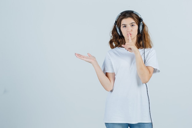 Jeune femme montrant le geste de silence, écartant la paume de côté en t-shirt blanc et regardant sensible, vue de face.