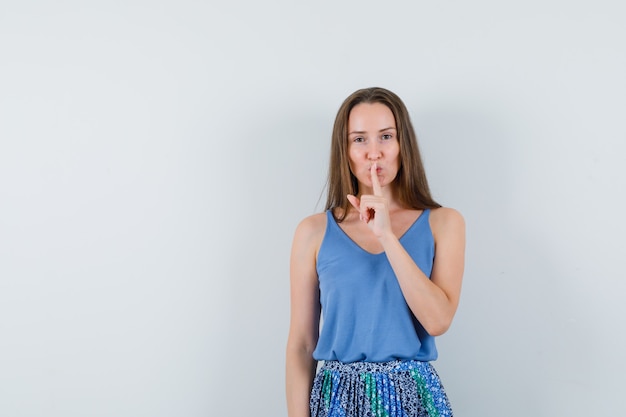 Jeune femme montrant le geste de silence en maillot, jupe et à la vue sensible, de face.