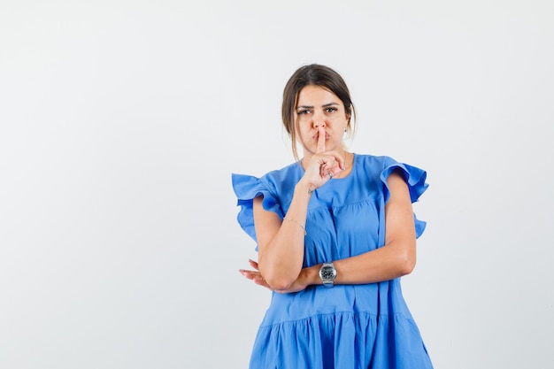 Jeune femme montrant le geste de silence en robe bleue et à la prudence