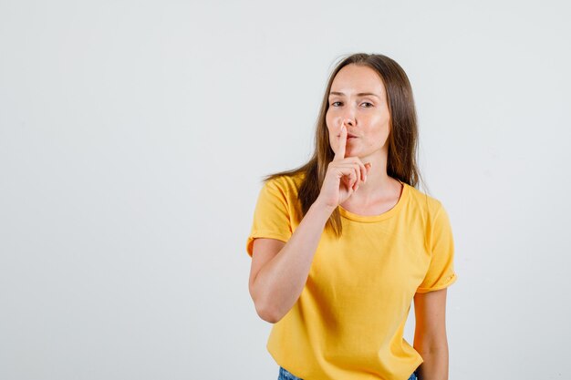 Jeune femme montrant le geste de silence et souriant en t-shirt, short vue de face.