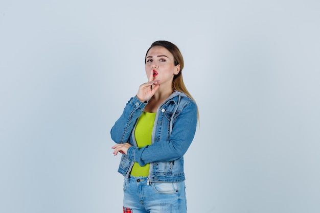 Jeune femme montrant un geste de silence en tenue de denim et semblant mystérieuse. vue de face.