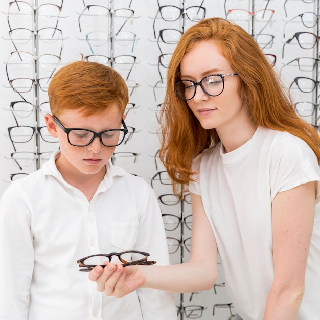 Photo gratuite jeune femme montrant des lunettes au garçon de taches de rousseur dans le magasin d'optique