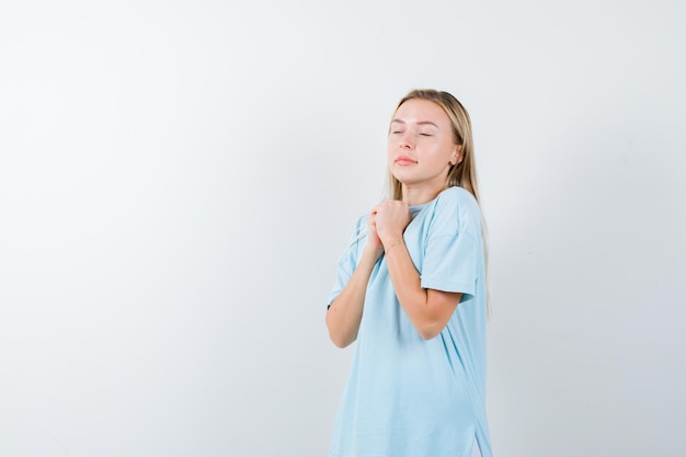 Jeune femme montrant les mains jointes dans un geste implorant en t-shirt et l'air paisible