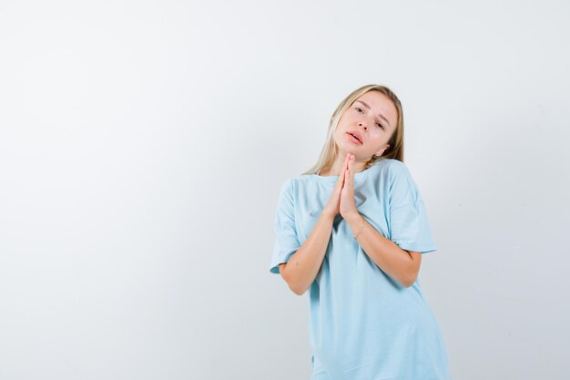 Jeune femme montrant les mains jointes dans un geste de plaidoirie en t-shirt isolé